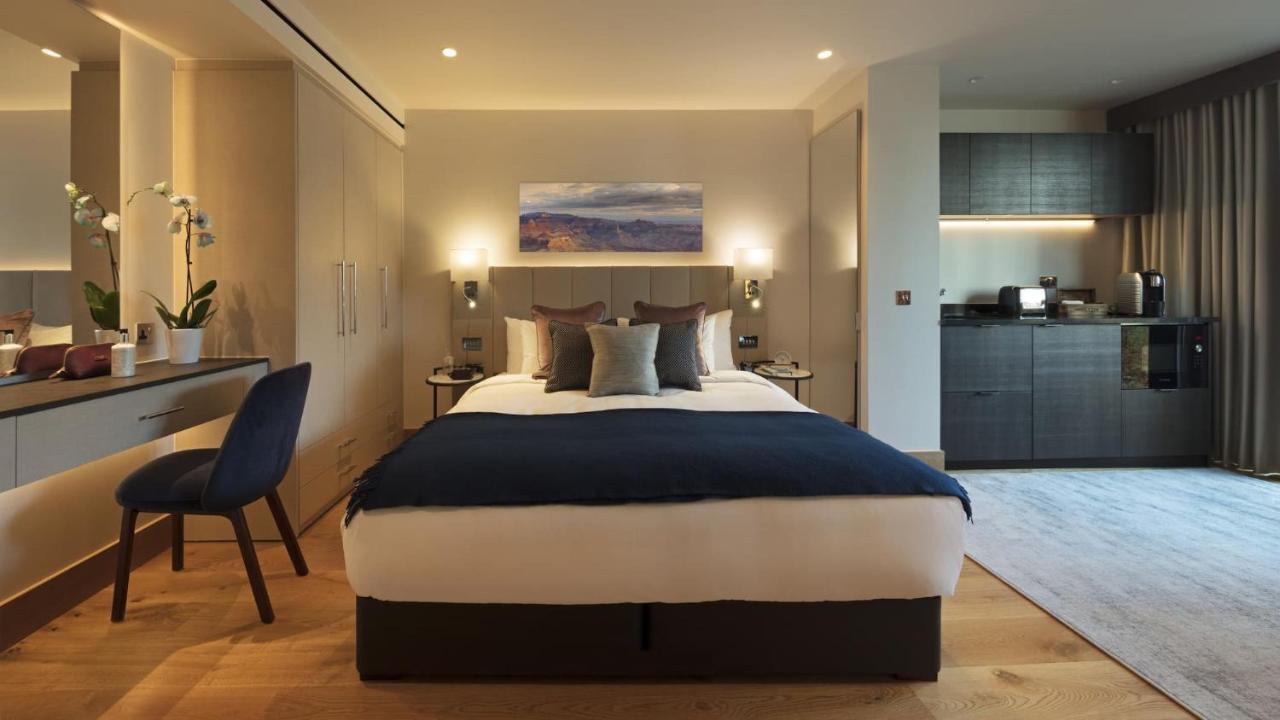 Tower Suites By Blue Orchid London Kültér fotó The photo displays a modern hotel room featuring a plush bed with a dark blue bedspread and several decorative pillows. The walls are adorned in neutral tones, and there is a piece of artwork above the bed depicting a serene landscape. On the side, t