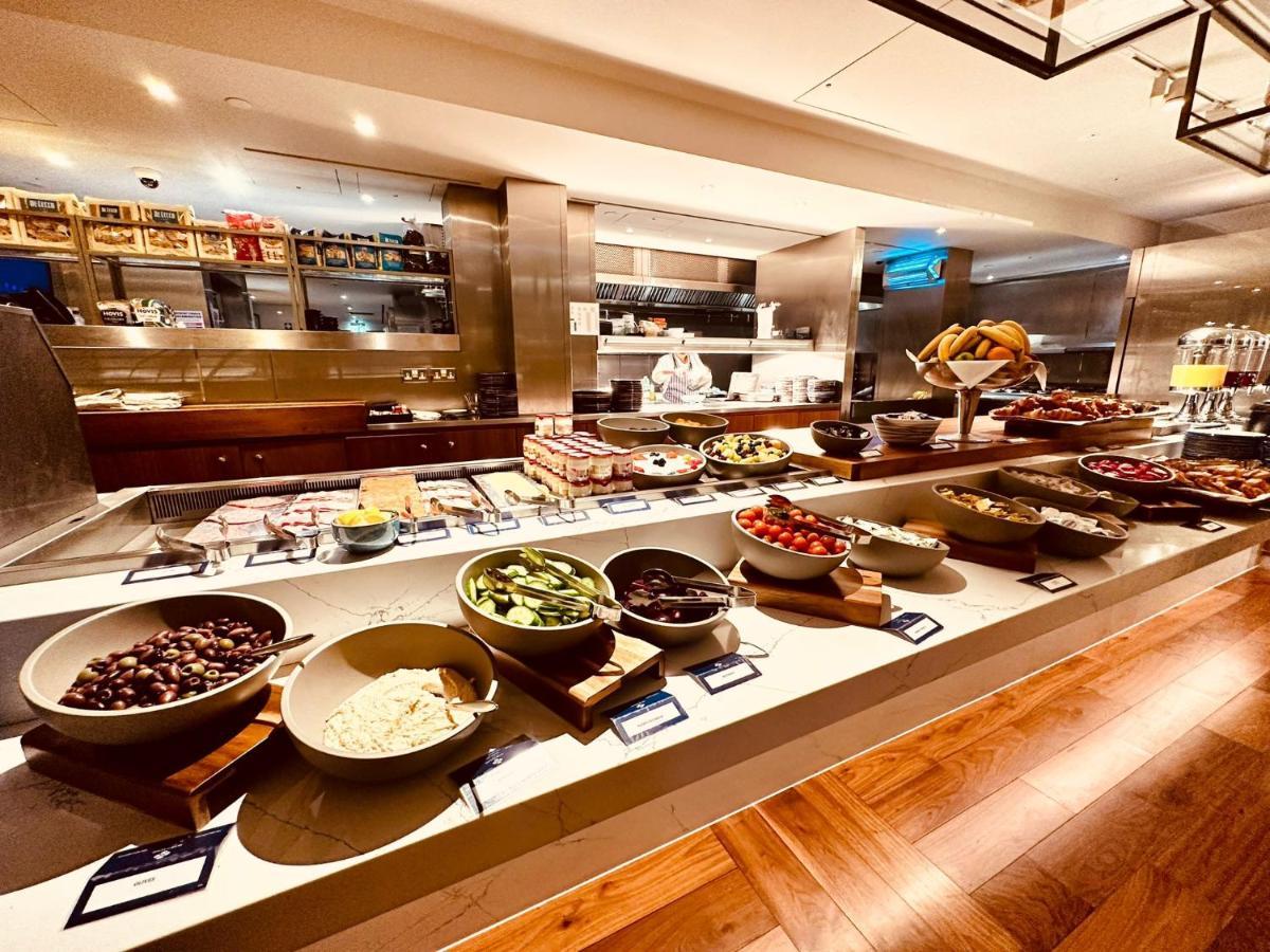 Tower Suites By Blue Orchid London Kültér fotó The photo shows a well-organized buffet spread. There are several bowls filled with various ingredients, likely for a meal or a salad bar. The ingredients include different types of vegetables, fruits, and possibly some grains or legumes. In the back