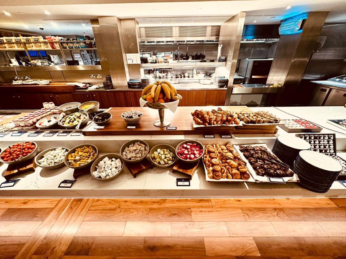 Tower Suites By Blue Orchid London Kültér fotó The photo displays a beautifully arranged buffet featuring a variety of food items. There are several bowls and platters filled with colorful fruits, pastries, and desserts. In the center, a large bowl of bananas is prominently placed. Surrounding th