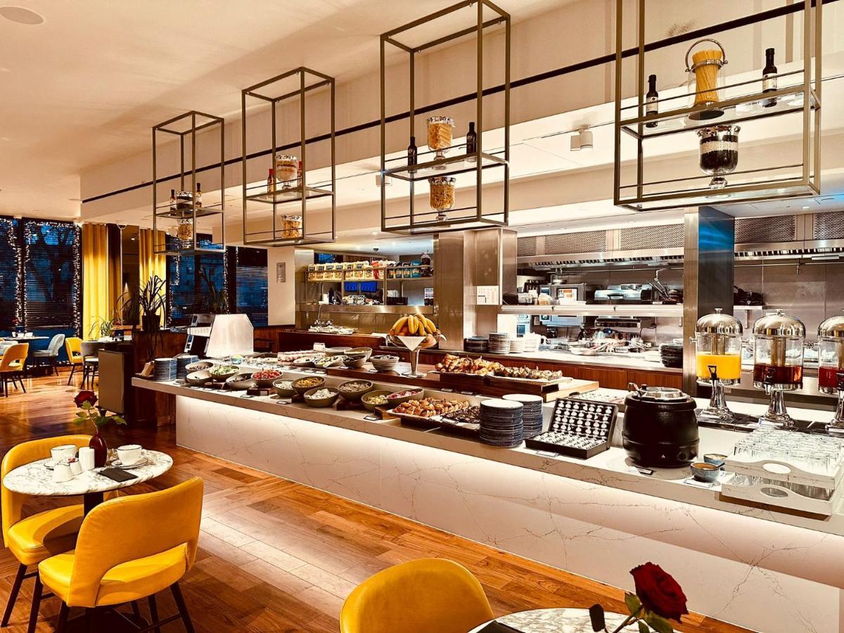 Tower Suites By Blue Orchid London Kültér fotó The photo shows a modern restaurant interior featuring a buffet layout. The space has a sleek design with wooden flooring and a bright, open atmosphere.  

The buffet counter is richly arranged with various dishes and food items, likely for a breakfa