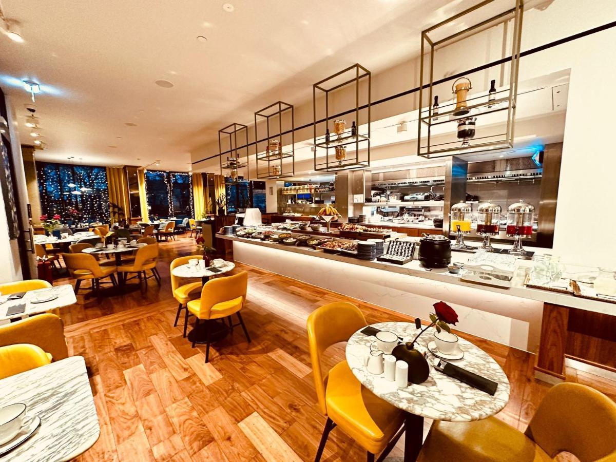 Tower Suites By Blue Orchid London Kültér fotó The photo depicts a modern restaurant interior with a spacious layout. There are several round tables, each adorned with marble tabletops and stylish yellow chairs. A buffet area is visible in the background, featuring various food setups and kitchen